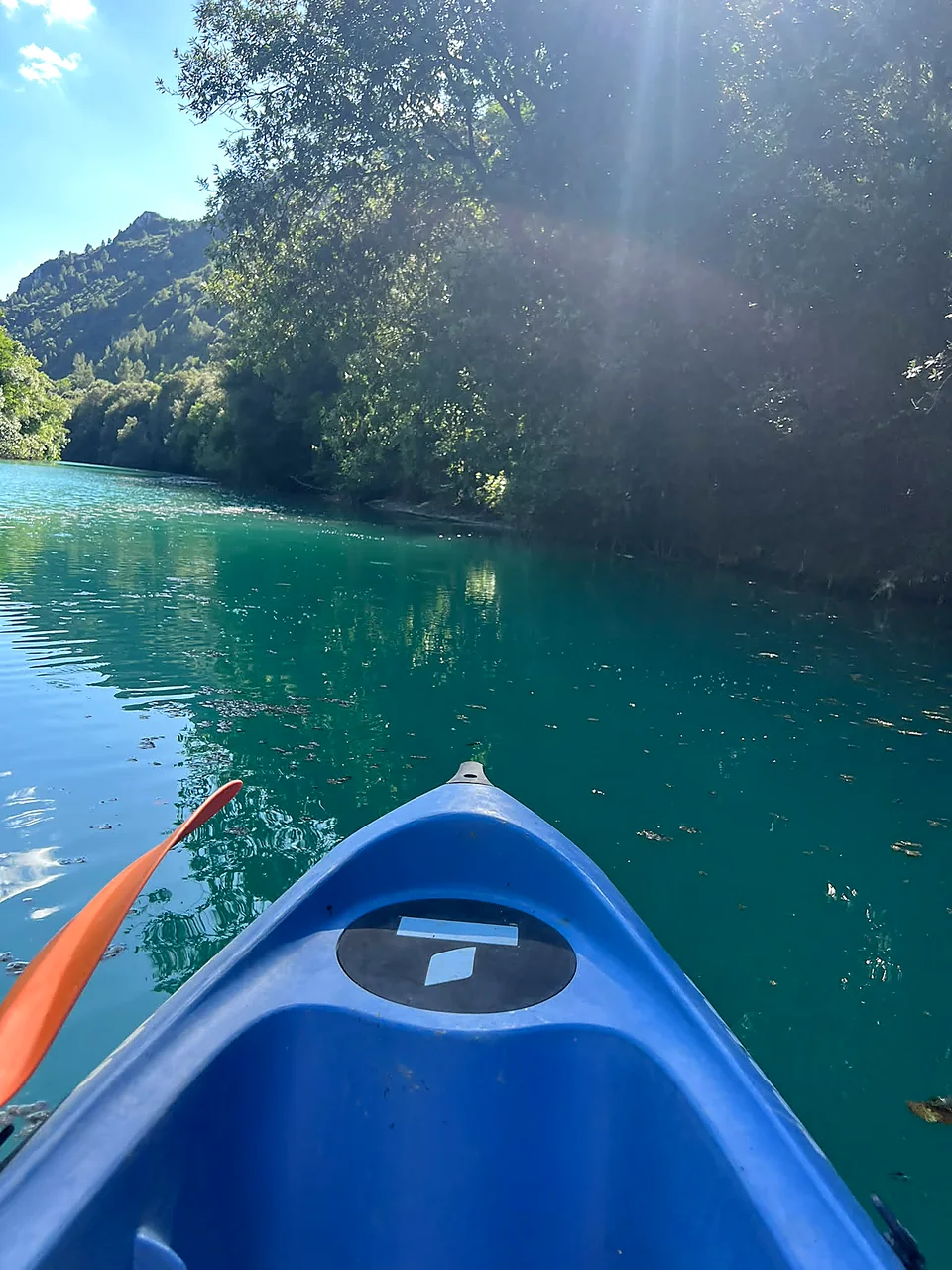Vista dalla prua della canoa blu sul fiume Nera turchese, raggi di sole tra gli alberi
