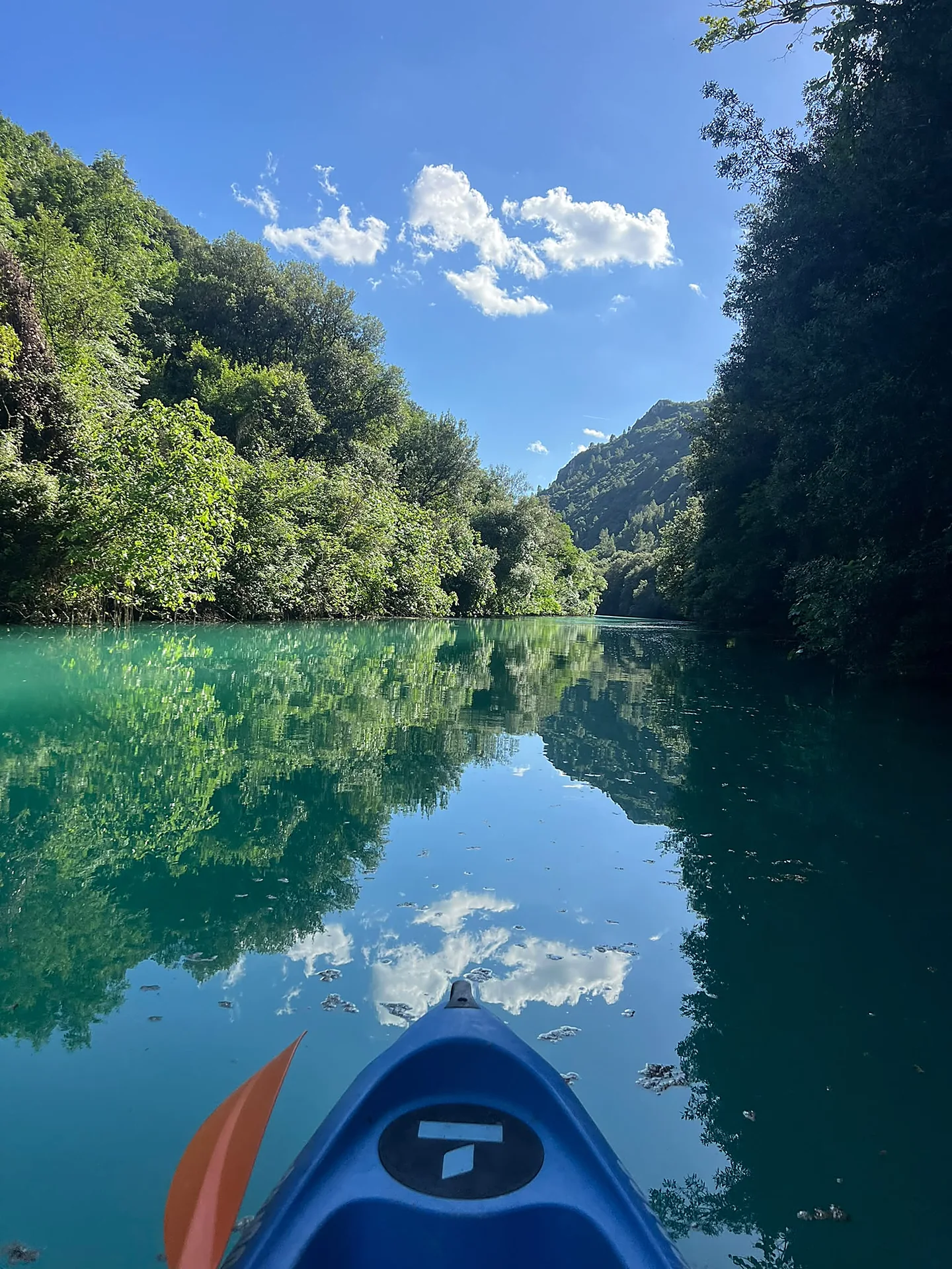 Canoa sul fiume Nera con riflesso perfetto delle nuvole sull'acqua turchese, vista dalla prua tra le gole
